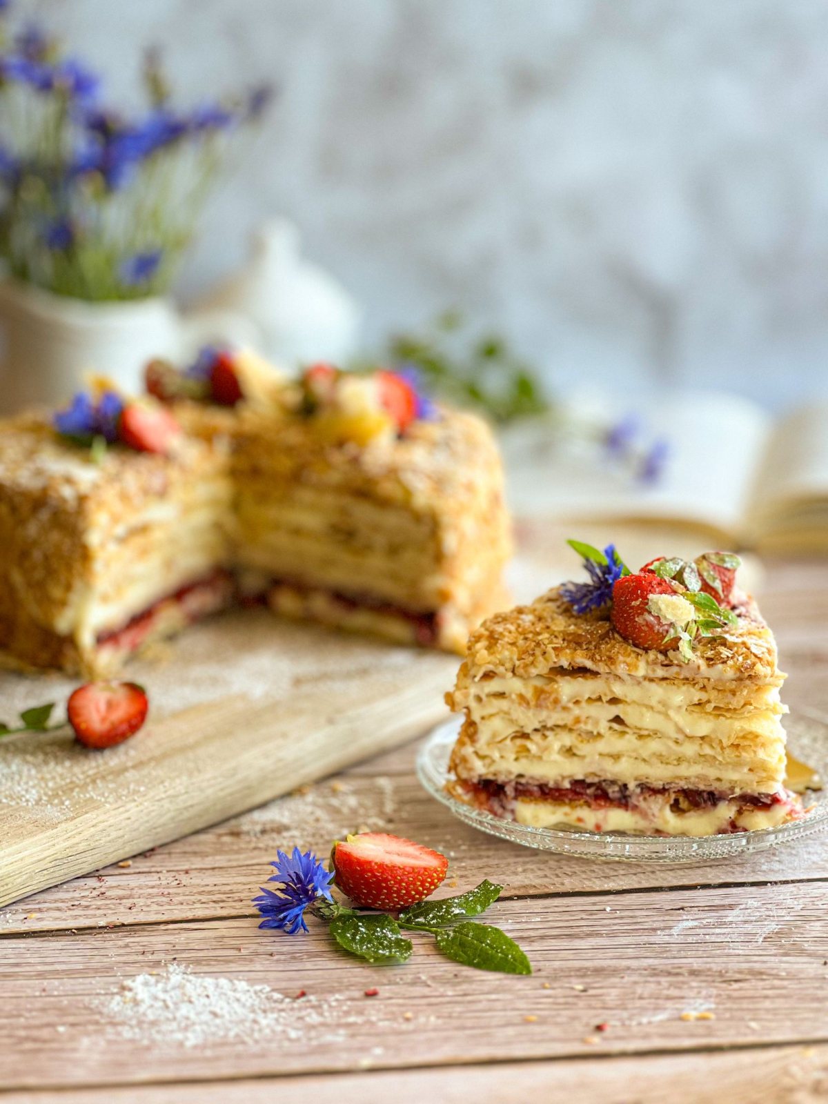 Qatlamli Napoleon tort bo‘lagi, ustida qulupnay va gullar